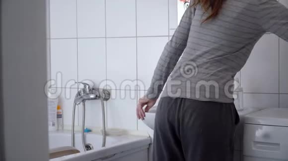 一个美丽的女人刷牙和在浴室里照镜子的肖像4k视频的预览图