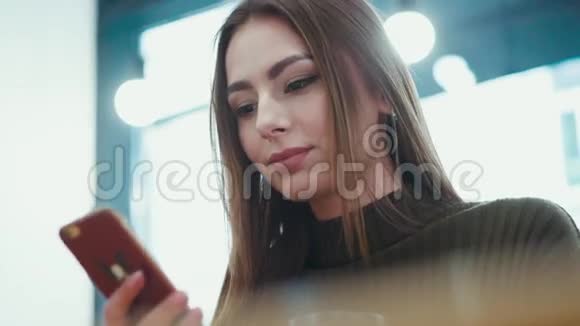漂亮的年轻女子穿着时尚的服装端着手机上网喝着咖啡坐着微微一笑视频的预览图