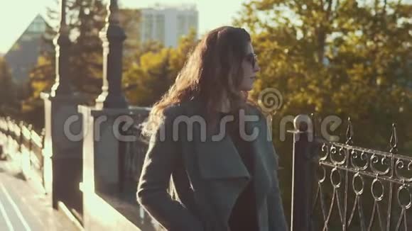 戴着太阳镜的迷人少女穿着外套微笑着穿过秋天的城市视频的预览图