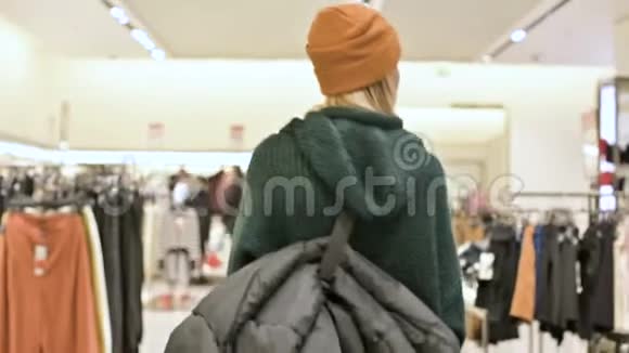 从后面的女孩穿着毛衣和帽子购物的视野穿过一家服装店现场摄像机视频的预览图