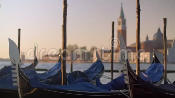 一幅覆盖着的贡多拉斯在码头上的特写映衬着模糊的威尼斯景色视频的预览图
