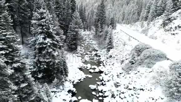 冬季雪中蜿蜒穿过森林的小溪和道路的鸟瞰图视频的预览图