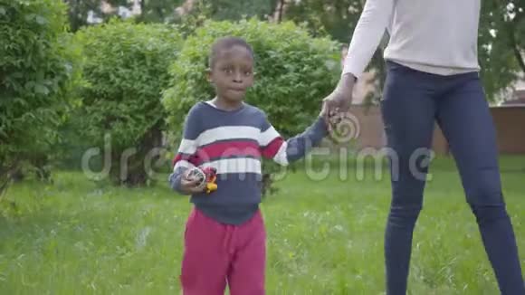 可爱的非裔美国女人和她的小儿子牵着手在公园里散步可爱的孩子在户外玩耍视频的预览图