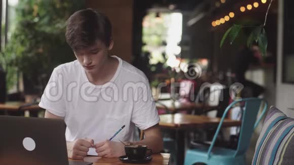 年轻学生在咖啡馆做作业自由职业者用铅笔在纸上画画现代工作场所坐在咖啡馆里视频的预览图