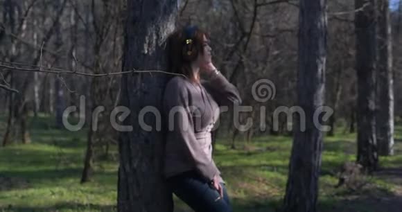 美丽的少女在耳机上听音乐在森林中享受大自然的自由与美丽视频的预览图