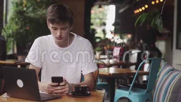 年轻人用带电线的耳机在咖啡馆里列出音乐现代工作场所坐在咖啡馆里打开笔记本电脑视频的预览图