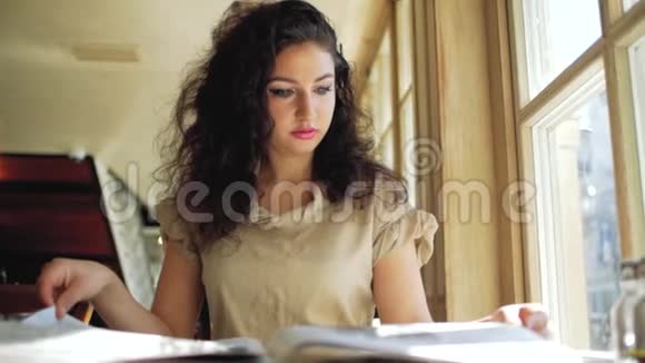 卷发的女人坐在一家咖啡馆的窗户附近从报纸上看到树叶视频的预览图