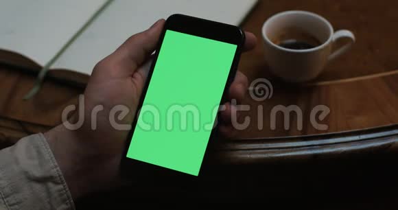男人拿着一部现代智能手机在一家咖啡馆里展示绿色屏幕桌子上放着一杯咖啡视频的预览图