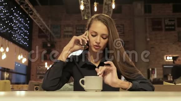 一位年轻的商务女士坐在咖啡馆的桌子旁用手机说话视频的预览图