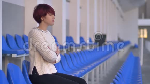 一幅无聊的美丽的粉红色头发女孩坐在体育场上用手臂等待着什么的画像视频的预览图