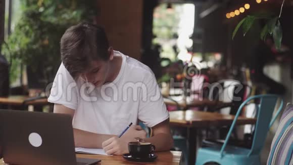 年轻学生在咖啡馆做作业自由职业者用铅笔在纸上画画现代工作场所坐在咖啡馆里视频的预览图