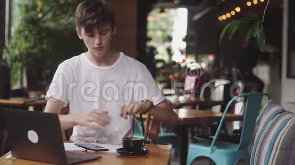 年轻人用带电线的耳机在咖啡馆里列出音乐现代工作场所坐在咖啡馆里打开笔记本电脑视频的预览图