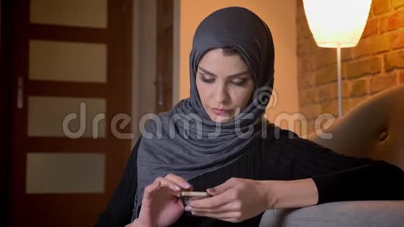 戴头巾的穆斯林成年女性的特写肖像坐在门口的地板上发短信视频的预览图