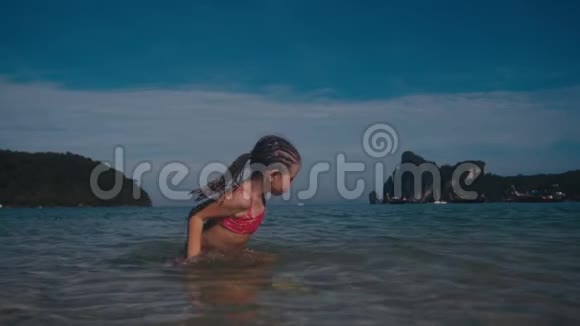 穿泳衣的小漂亮女孩在温暖的夏天的海洋里玩耍泼水视频的预览图