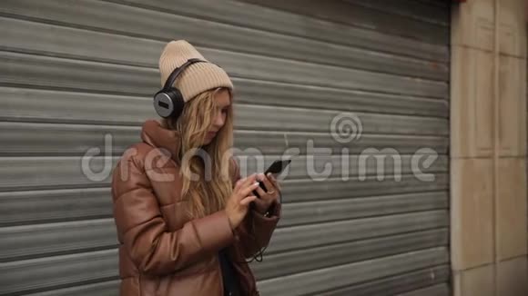 笑着笑着英俊的年轻女子戴着耳机听着智能手机里的音乐在街上跳舞视频的预览图