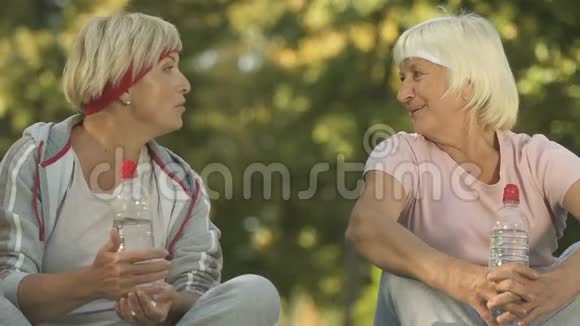 两个穿运动服装的女朋友在外面锻炼后聊天坐在公园里视频的预览图
