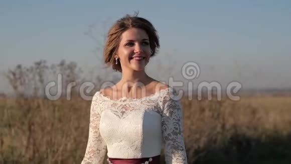 在一个阳光明媚的日子里一个女人穿着白色的裙子在大自然的背景下穿过一片田野视频的预览图