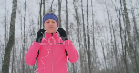 晨冬慢跑前的女人在耳朵里插入耳机准备穿过自然公园视频的预览图