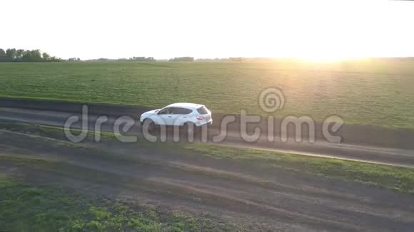 汽车沿着地面公路行驶经过明亮的夕阳下的田野视频的预览图