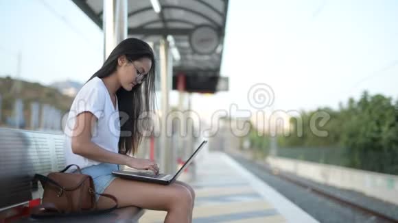 年轻快乐的亚洲旅游妇女坐着用笔记本电脑等火车视频的预览图