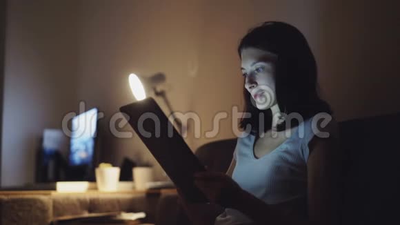 年轻漂亮的女人晚上在家里用平板电脑购物视频的预览图