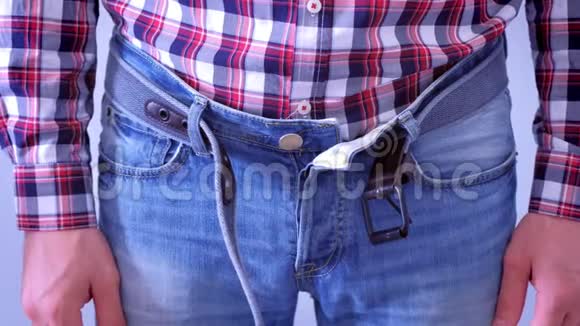 男人几乎不扣牛仔裤的腰带拉着肚子双手特写视频的预览图