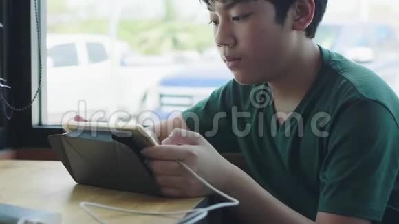 亚洲小男孩在咖啡馆的触摸板上享受游戏视频的预览图