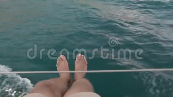 年轻人坐在一艘移动游艇的甲板上双腿在空中摆动视频的预览图