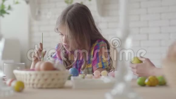 妈妈和小女孩用颜色和刷子给复活节彩蛋着色准备复活节假期一个幸福的家庭视频的预览图