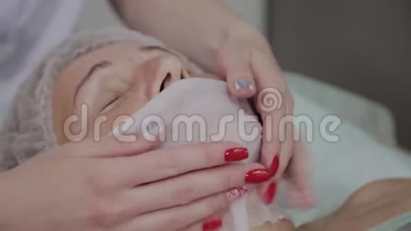 专业美容师在美容办公室对一位老年妇女的脸上施加擦拭视频的预览图