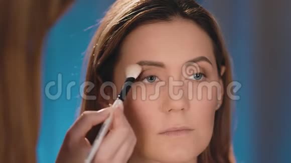 化妆师在眼皮上抹黑在一个白人金发模特的脸上用专业的白色画笔视频的预览图