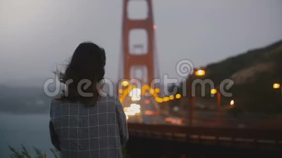 傍晚时分年轻的千禧一代学生独自站在黑暗的夏季傍晚观看标志性的金门大桥交通视频的预览图
