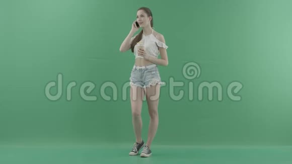 女人在绿色背景下喝鸡尾酒时打电话视频的预览图