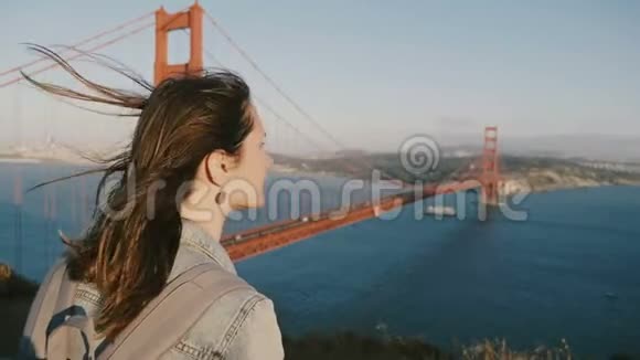 宁静的年轻旅游妇女头发在大风中吹拂在标志性的金门大桥欣赏史诗般的日落全景视频的预览图
