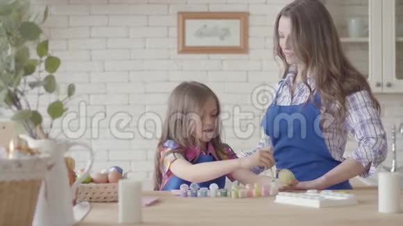 用刷子在厨房的桌子上画一个留着长发的可爱女孩画复活节彩蛋漂亮的女人视频的预览图