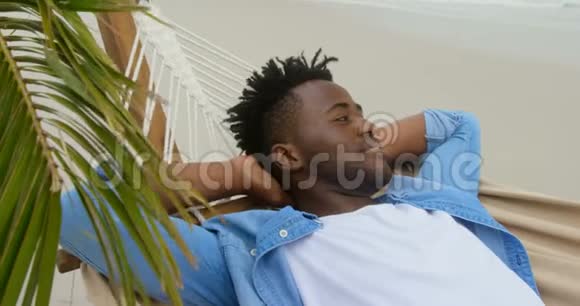 美国黑人男子在海滩上的吊床上放松的侧面景色视频的预览图