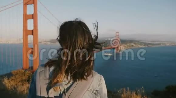 年轻的旅游妇女带着背包和头发在大风中吹着在旧金山金门大桥欣赏日落视频的预览图