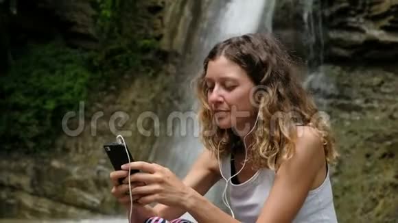 女人用耳机听音乐用智能手机对付一个大瀑布视频的预览图