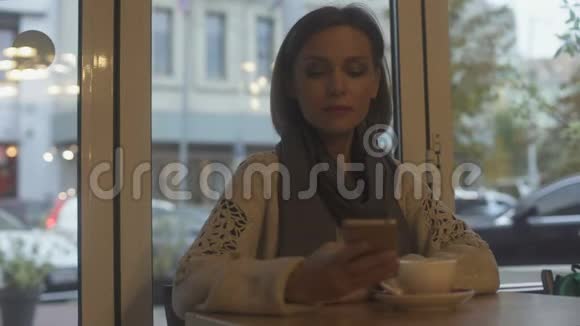 优雅的女人坐在咖啡馆里喝茶用智能手机回复电子邮件视频的预览图