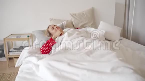 早上好美丽迷人的年轻女人姜发躺在床上躺在白色的被子下伸展举起手臂视频的预览图