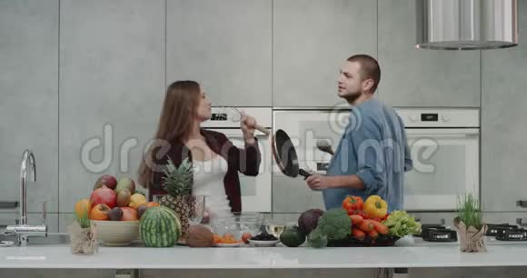 两个有魅力的年轻女士和家伙在厨房边准备食物边跳舞和唱歌早上伙计视频的预览图