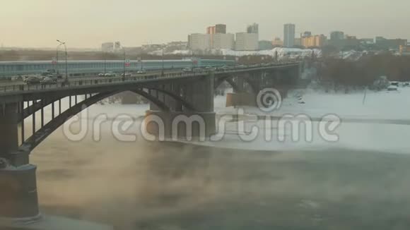 蒸汽在冰雪覆盖的河流上升起汽车在桥上行驶好日子视频的预览图