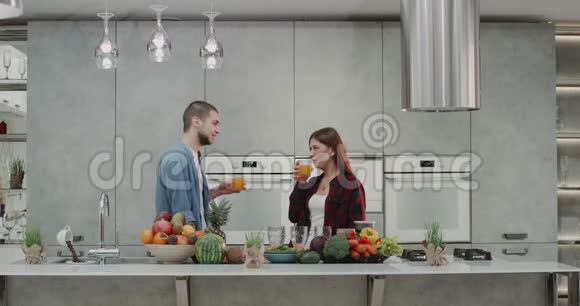 美丽的年轻夫妇早上在厨房里喝橙汁他们开心地笑着吃了一桌丰盛的橙汁视频的预览图