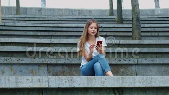 一个公园里年轻漂亮的女孩手里拿着一部智能手机写着一条信息在电话里翻出照片视频的预览图