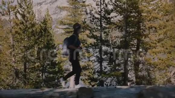 侧观看年轻的当地女孩徒步旅行与背包在美丽的岩石在约塞米蒂国家公园森林湖慢动作视频的预览图
