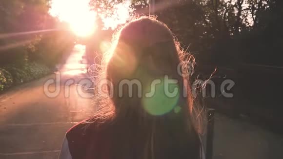 年轻的金发少女在惊人的日落中行走美丽的女孩走在路上后景暖光粉红色视频的预览图