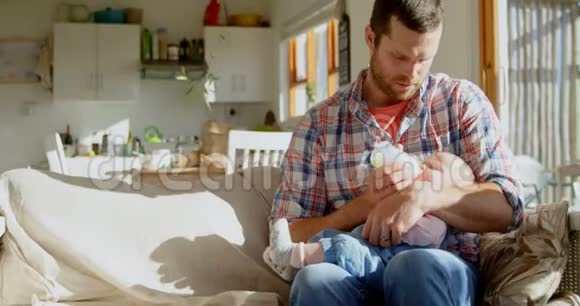 在一个舒适的家中从瓶子里给孩子喂奶的中白种人父亲的正面景色视频的预览图