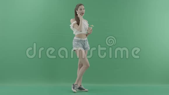 年轻的美女一边喝着绿色背景的鸡尾酒一边打电话视频的预览图