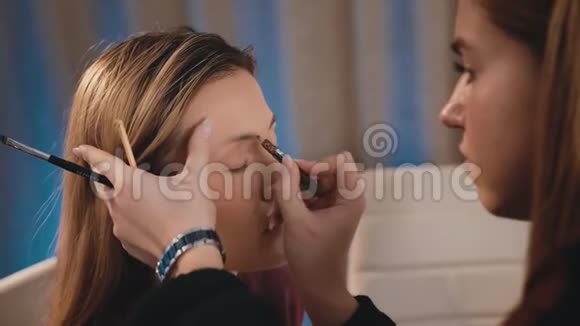 白种人的化妆师用铅笔在白种人金发的脸上画和诱导眉毛的形状视频的预览图
