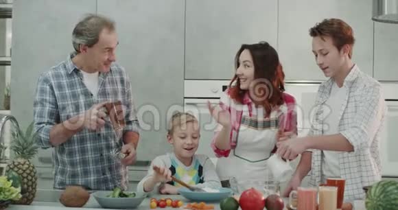 有魅力的家庭在周末一起在现代化的厨房里做早餐四个家庭成员在一起度过美好的时光视频的预览图